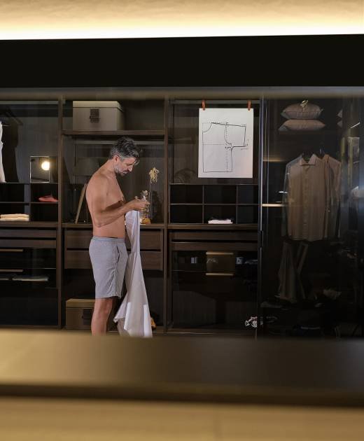 Side view mature man with naked torso standing near wardrobe and looking at white shirt in hands before putting on